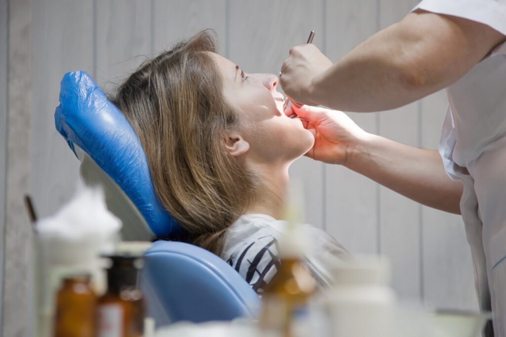 A dentist examining a woman’s teeth during a routine dental checkup as she reclines in a dental chair.